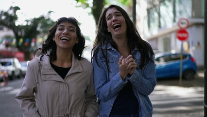 Female friends laughing and smiling while while walking in city sidewalk. Authentic real expression laugh and smile
