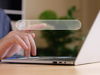 Man use finger touch virtual search bar with internet searching concept. Laptops is on wood table in front of a man.