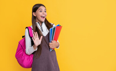 amazed child with school backpack and workbook on yellow background