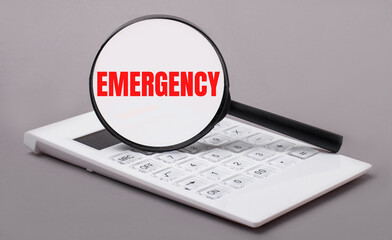On a gray background, a white calculator and a magnifying glass with the text EMERGENCY. Business concept
