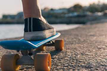 Close-up image of a young man's foot on a penny longboard by the sea or on the promenade at sunset. Alternative concept of sport among middle-aged people.