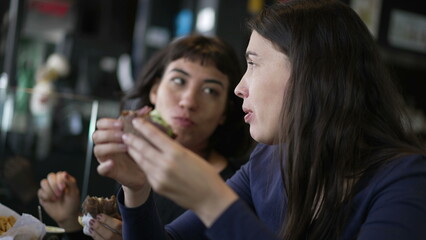 Two young women eating hamburgers. People at restaurant taking a bite of burgers