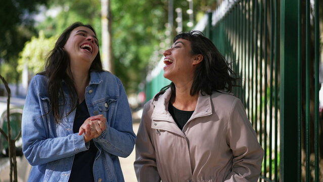 Two happy female friends walking outside. Carefree girls walk in urban street together