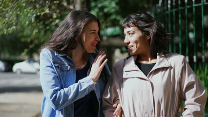 Two female friends gossiping walking together pointing with hand. Friend sharing gossip