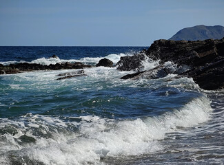 Fototapeta na wymiar summer fun dynamic waves breaking on rocks blue sky and sunshine