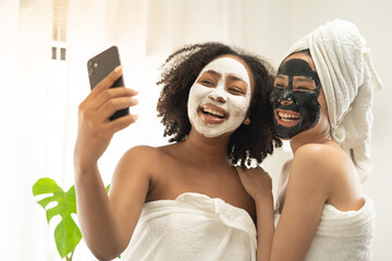 Pretty couple Asian African woman close friend smile fun and selfie together with masking face spa...