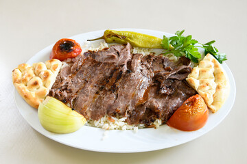 Turkish and Arabic Traditional Ramadan doner kebab with tasty tomato sauce and rice or turkish pilav in white plate on wood table background. ( Pilav ustu doner)