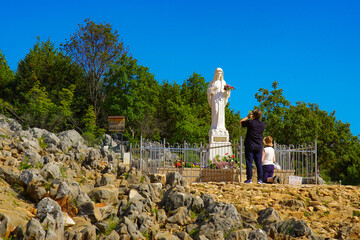People praying in front of the statue of the Mother of God in the place of her apparitions -...