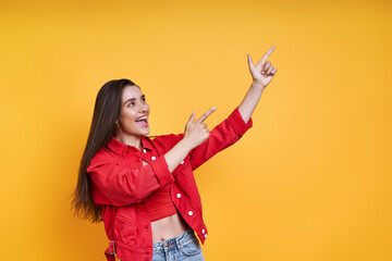 Excited young woman pointing away while standing against yellow background