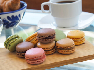 Colorful french macaroons on a wooden board with a cup of coffee. 
Vintage style, aesthetic   
