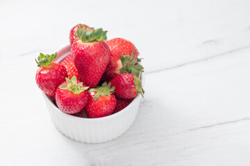 Fresh ripe delicious strawberries in a white bowl on a gray stone background