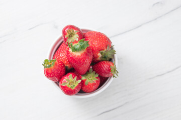 Fresh ripe delicious strawberries in a white bowl on a gray stone background