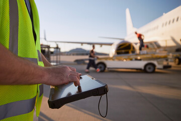Member of ground crew preparing airplane before flight. Worker using tablet against plane at...