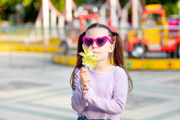 a child girl in an amusement park in the summer blows on a toy spinner near the carousels in...