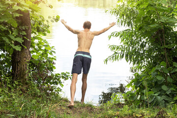 Young man at the lake just before jumping into the water in sunlight. Sport, fitness, swimming outdoors in nature, healthy lifestyle