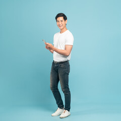 Nice asian guy in white t-shirt and jeans holding smartphone isolated on blue background