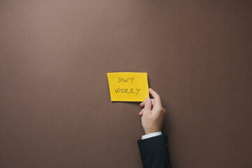 Businessman placing yellow paper with Dont worry sign over brown background