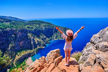 Free carefree joyful girl traveler with open arms stands on hill rock over sea bay in Turkey, butterfly valley. Enjoy travel concept