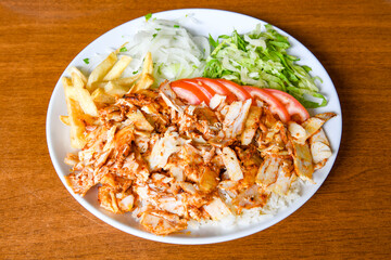 Turkish and Arabic Traditional Ramadan doner kebab with tasty tomato sauce and rice or turkish pilav in white plate on wood table background. ( Pilav ustu doner)