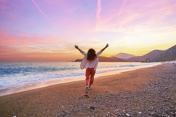 Happy carefree one alone joyful girl running with open arms on the beach at sunset. Beautiful moment life vacation
