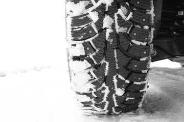 Winter studded tire on white snow as symbol of safe driving on winter tires in winter andneed to...