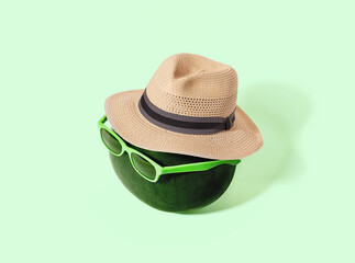 Watermelon with sunglasses and straw hat on green pastel background