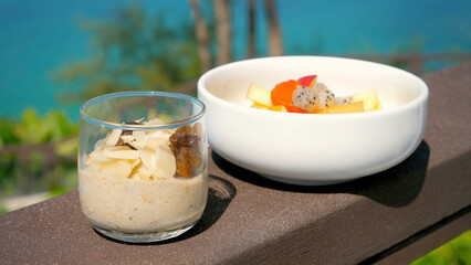 Healthy tropical breakfast with oatmeal and exotic fruits. Vacation in Thailand in modern resort with sea view on background. Vegan food, clean eating, diet or detox concept.