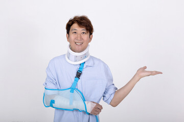 Portrait of smiling Asian man with broken arm and neck showing empty space isolated on white...
