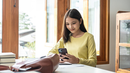 Young woman student in sweater is using smartphone to chatting with classmate while taking a break