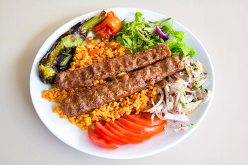 Grilled Turkish Adana, Urfa  Kebab with grilled vegetables, onion and rice on plate. Adana durum .