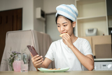 Woman is having breakfast with crackers mixed with various grains and using mobile phone to update her morning news, Small room in condominium background, Wake-up activities