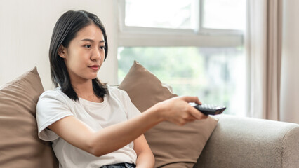 Half-Japanese woman turns on the TV to watch a movie or drama in the living room, Hold the remote to turn on-off the TV, Relaxing time on vacation, happy corner, Remote control