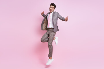 Happy young man in full suit jumping against pink background