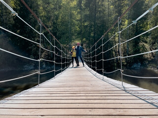 Fototapeta premium A man on a suspension rope bridge over a river. Beautiful landscape and traveler portrait