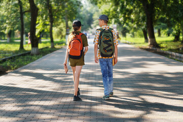 portrait of students in a city park, teenage schoolchildren a boy and a girl walking along a path, rear view