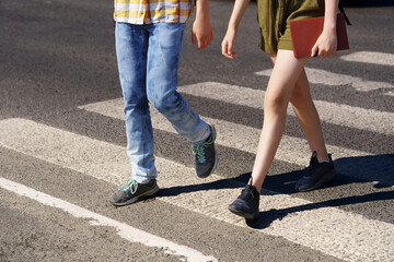 teenage schoolchildren, a boy and a girl cross the road at a pedestrian crossing