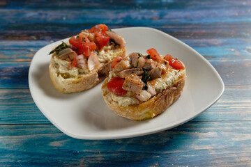 Crostini with eggplant cream and herring salad with tomato. Served on white plate and blue wooden table.