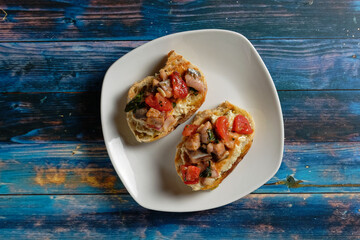 Crostini with eggplant cream and herring salad with tomato. Served on white plate and blue wooden table.