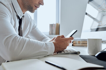 Close-up of man in shirt and tie using smart phone while sitting at his working place in office