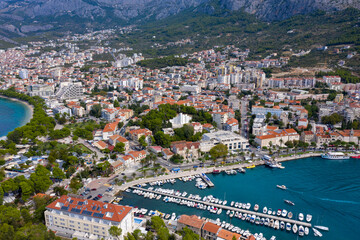 View of the harbor and city. Makarska riviera.Dolmatia.Blue south sea. Mountains, houses, yachts, ships, boats on the pier. City beach and pier. Drone footage. Summer. Adriatic. Relax. Vacation. 