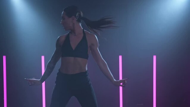 Attractive talented woman dancing on pink and blue neon background in studio. Graceful female dancing in studio with smoke and spotlight. Slow motion in 4K, UHD