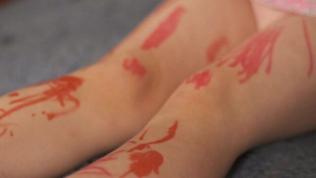 Little child draws with red marker on his arms and legs. Creative kid. Happy childhood. Close up.