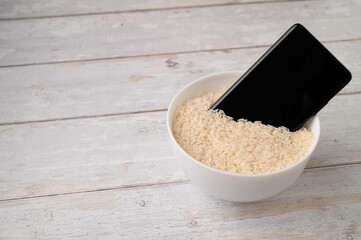 A mobile phone placed to dry in a bowl full of rice after the phone fell into water. Light wooden...