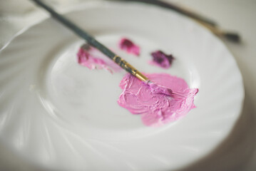 pink oil paints with brushes on a white plate on the table side view close-up