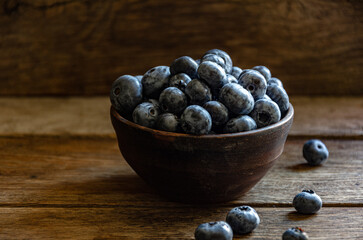 Blueberries in a clay cup, on a wooden table. Ripe berries in the kitchen, harvest.
