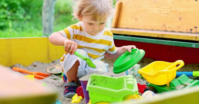 A little boy playing in the sandbox at the playground outdoors. Toddler playing with sand molds and making mudpies. Outdoor creative activities for kids
