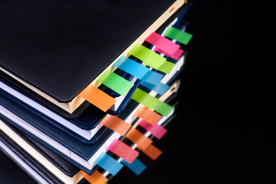 Close-up of a stack of office notepads with colorful sticky page markers sandwiched between pages on dark background