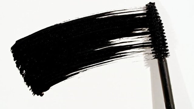 Macro shot and slow motion of a black mascara isolated on white background. Advertising professional cosmetics. Closeup of a mascara wand on white background. High quality 4k footage