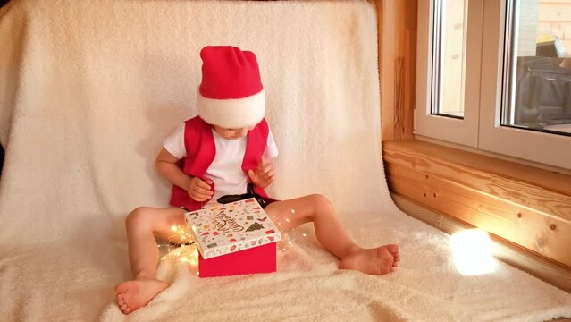 Little boy in Santa Claus costume opened gift box with black rabbit and delighted. Childhood with pet love. Merry Christmas celebration. Hare is the symbol of 2023 by the eastern calendar. Happiness.