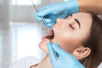 Fototapeta premium A dentist doctor treats caries on a tooth of a young beautiful woman in a dental clinic. Tooth filling.